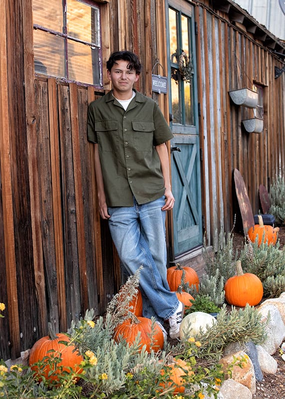 Evoto young man leaning on rustic building with pumpkins